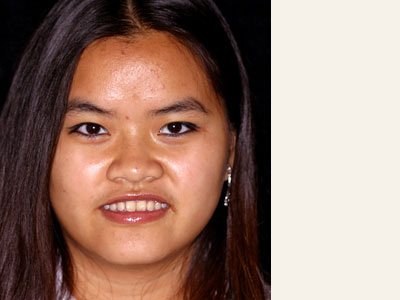 The image is a close-up portrait of an individual with medium to long hair, wearing makeup and a necklace, against a neutral background.
