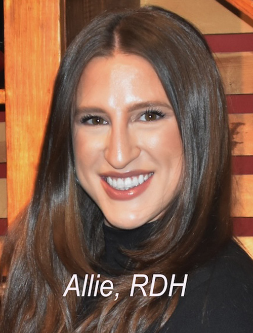 The image shows a woman posing for a photograph. She is smiling and has her hair styled straight.