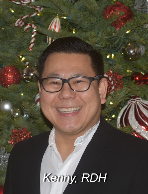The image shows a man standing in front of a Christmas tree, smiling at the camera. He is wearing glasses and has short hair. In the bottom right corner of the image, there is text that reads  Kenny, RDH .