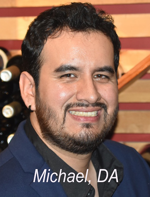A man with a beard and mustache, wearing a suit jacket, is smiling at the camera.