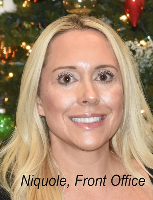 A woman posing for a photo in front of a Christmas tree, smiling and looking directly at the camera.