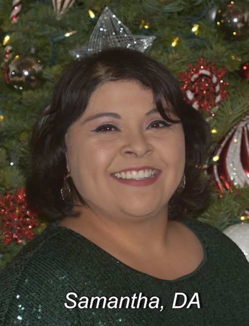 Woman posing in front of a Christmas tree, smiling and wearing makeup.