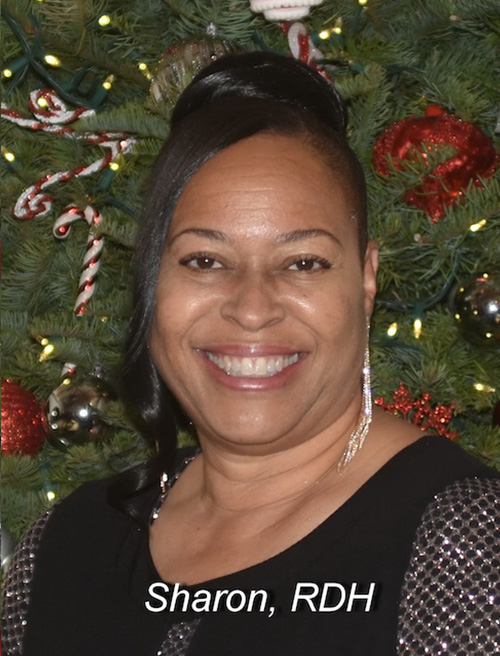 A smiling woman in a festive setting, standing in front of a Christmas tree.