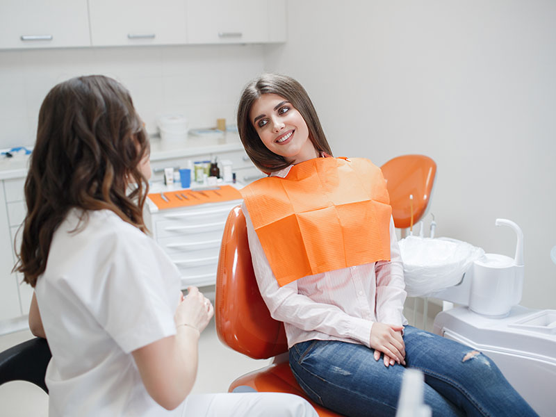 Woman in orange dental mask receiving treatment, seated next to dentist chair.