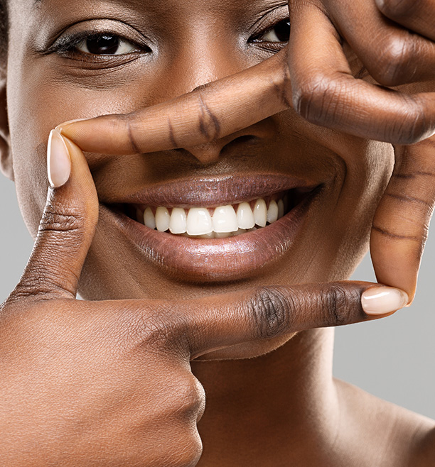 A woman with a radiant smile, holding up fingers to frame her face.