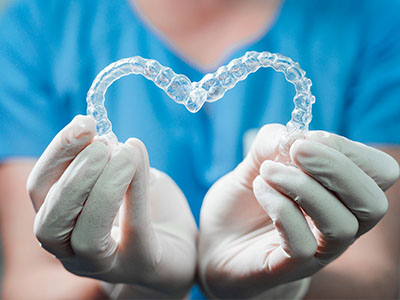 An image featuring a dental implant in the shape of a heart held by a person wearing medical gloves, set against a blurred background.