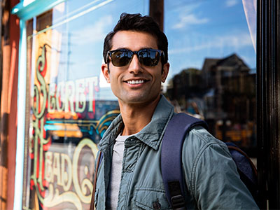 A man in sunglasses, a backpack, and a jacket is standing outside a storefront with a sign that reads  Sweet Treats.