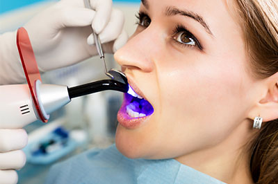A woman receiving dental treatment, with a dentist using an ultrasonic cleaning device and purple dye to clean her teeth.