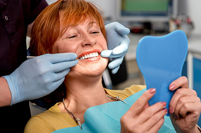 A woman in a dental chair, smiling and holding up a blue model of her teeth.