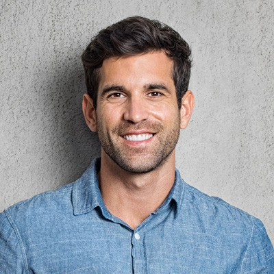 A man with a beard, smiling at the camera, poses for a portrait against a gray background.