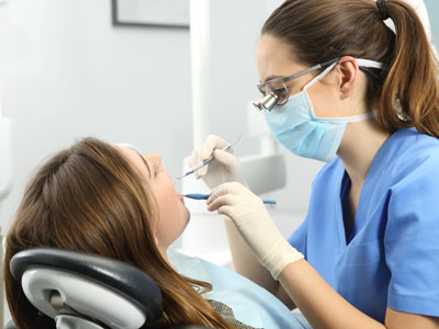 The image shows a dental professional in the process of performing a dental procedure on a patient, with the patient seated in a dental chair and wearing protective eyewear.