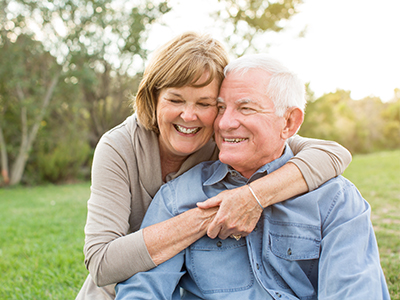 The image is a photograph of an elderly couple, both smiling and embracing each other, with the man wearing a blue shirt.