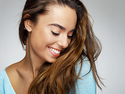 The image features a young woman with long hair, smiling gently, and looking to the side. She is wearing a light blue top.