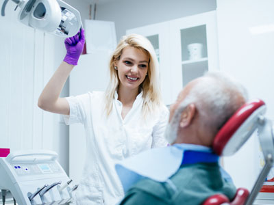 A dental professional in a white coat and purple gloves is assisting an elderly man with a medical device, possibly a dentist s chair or a dental machine, in a dental office setting.